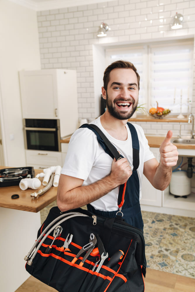 Bild von jungen Klempner Mann mit Ausrüstung Gestik Daumen nach oben in der Wohnung